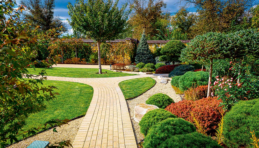 Ein gepflegter Gartenweg führt durch üppiges Grün, Sträucher und Beete.